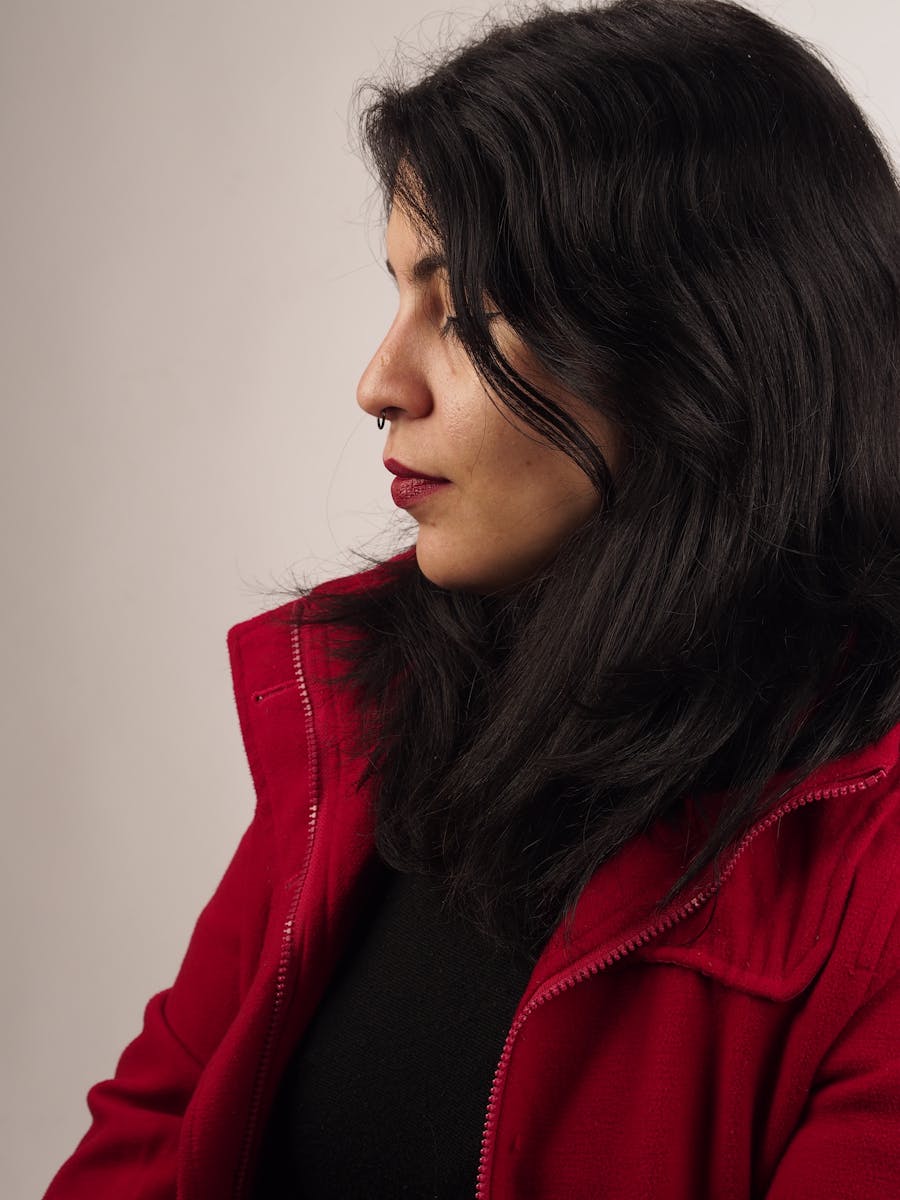 Side profile of a woman with dark hair in a red jacket, studio setting.
