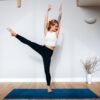 woman in white tank top and black leggings standing on blue yoga mat