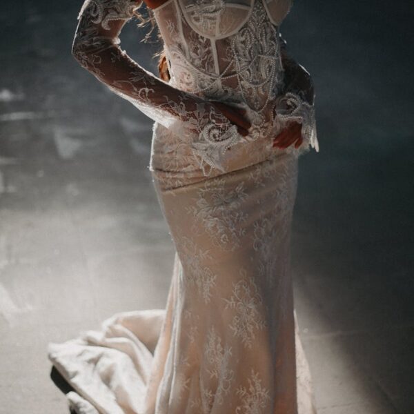 A beautifully detailed lace wedding dress worn by an adult female in soft, dramatic lighting.