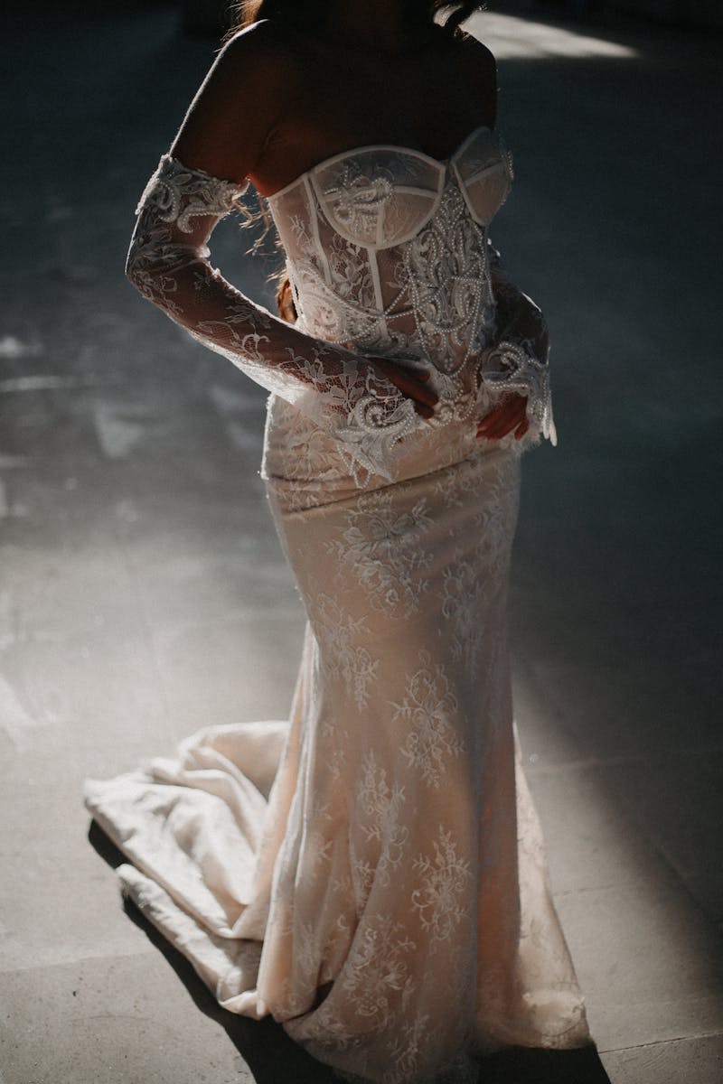 A beautifully detailed lace wedding dress worn by an adult female in soft, dramatic lighting.