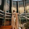 Graceful woman in a satin dress poses on a luxurious indoor staircase, surrounded by modern architecture.