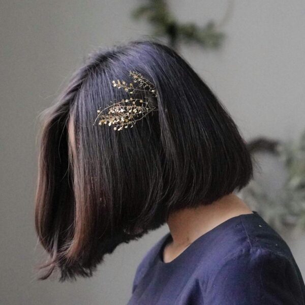 Profile view of a woman with a bob haircut adorned with a gold hairpin, against a neutral background.