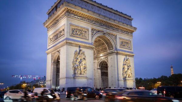 Iconic Arc de Triomphe under blue evening sky with bustling traffic in Paris.