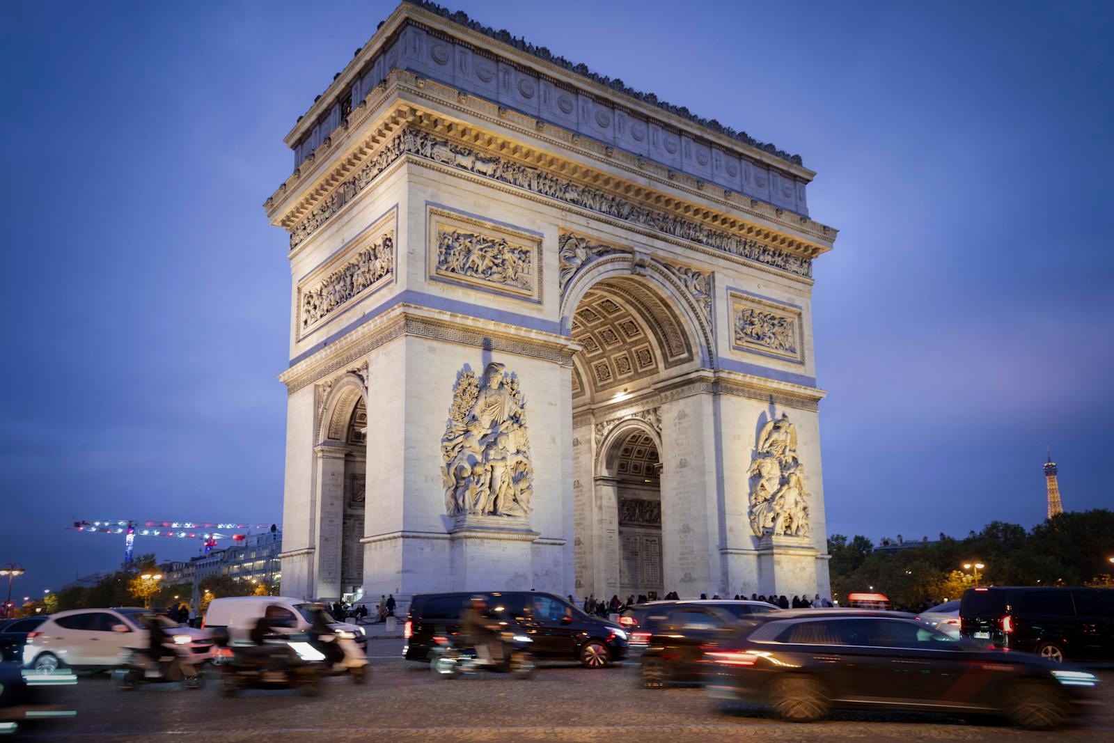 Iconic Arc de Triomphe under blue evening sky with bustling traffic in Paris.