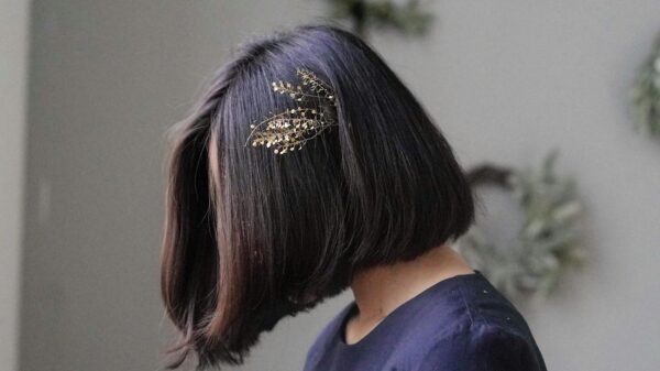 Profile view of a woman with a bob haircut adorned with a gold hairpin, against a neutral background.