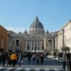 Crowds gather at St. Peter's Basilica, a landmark of Vatican City, under the daytime sky.