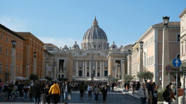 Crowds gather at St. Peter's Basilica, a landmark of Vatican City, under the daytime sky.