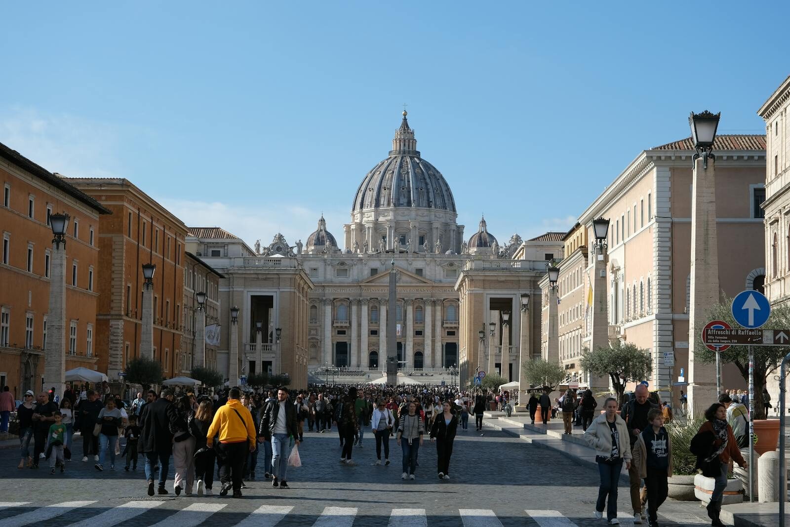Crowds gather at St. Peter's Basilica, a landmark of Vatican City, under the daytime sky.