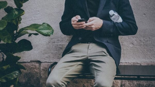 man using smartphone sitting on black metal bench near brown concrete wall