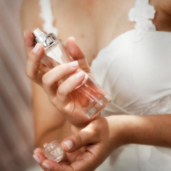 An elegant bride in a white gown applying perfume, capturing a moment of grace and preparation.