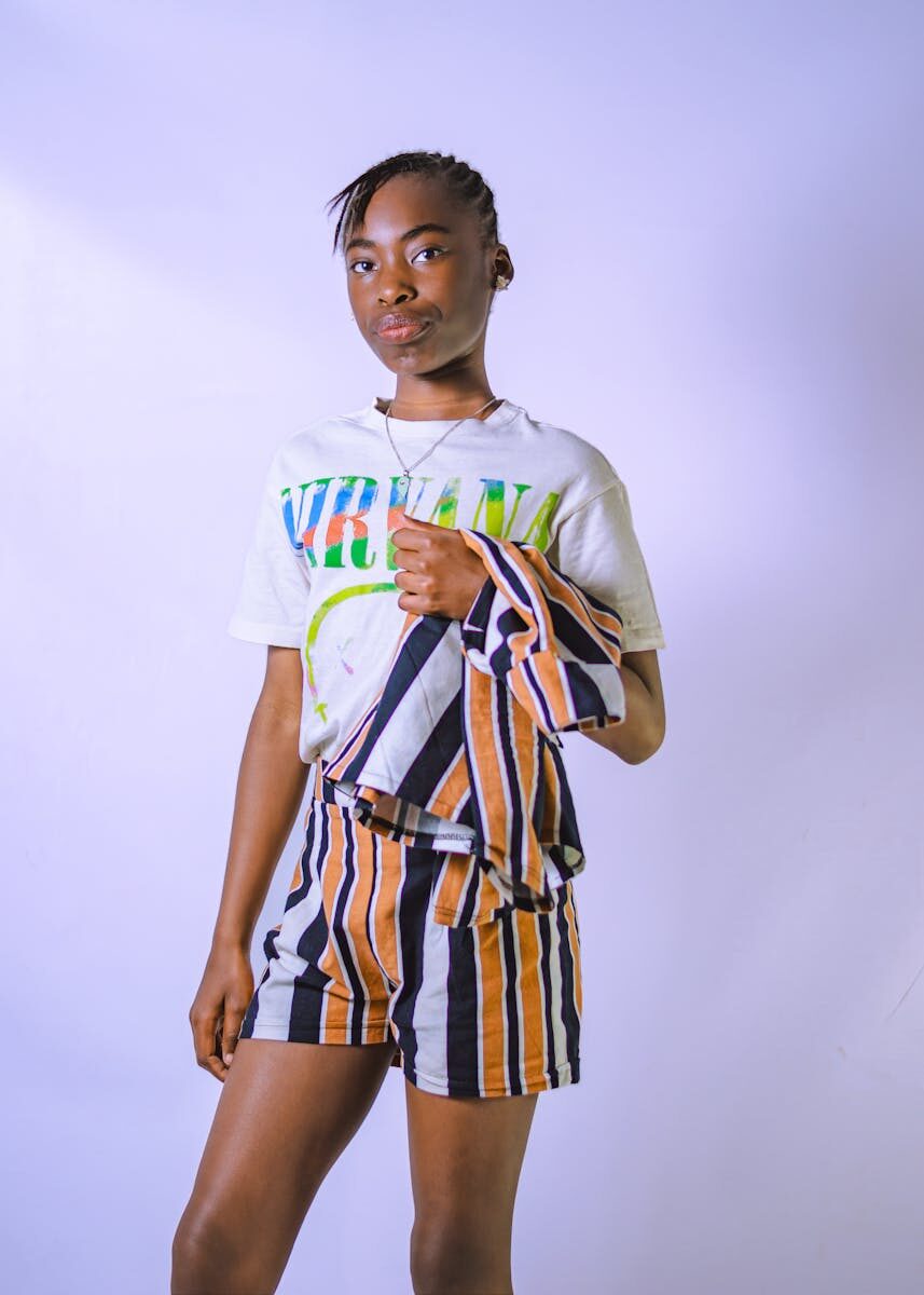 Teenage model poses confidently in a stylish striped ensemble against a white backdrop, exuding modern fashion vibes.
