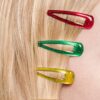 Crop anonymous female with red green and yellow hair clips on head on beige background