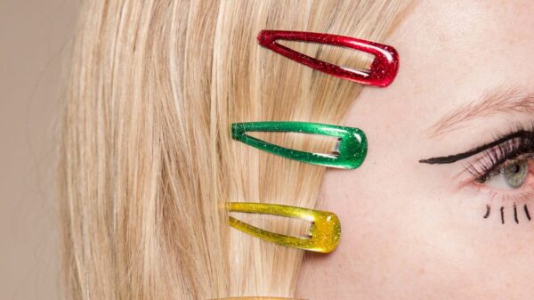 Crop anonymous female with red green and yellow hair clips on head on beige background