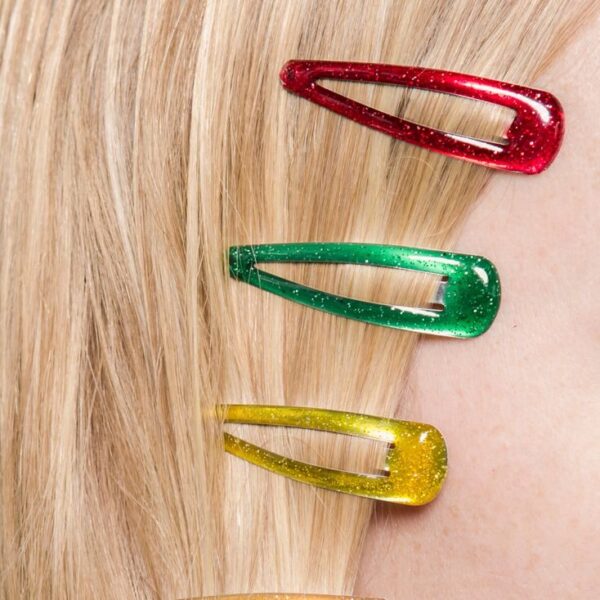 Crop anonymous female with red green and yellow hair clips on head on beige background