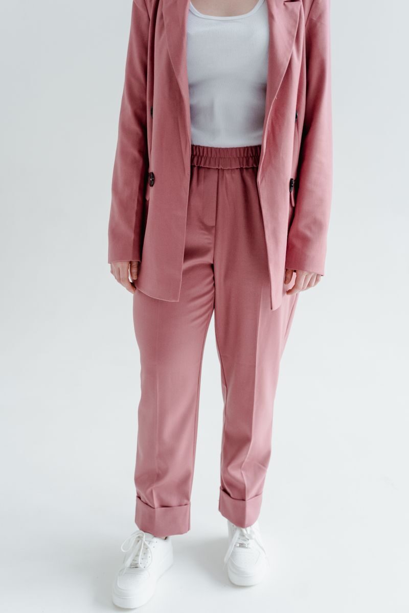 Confident woman in a stylish pink blazer and pants with white sneakers.