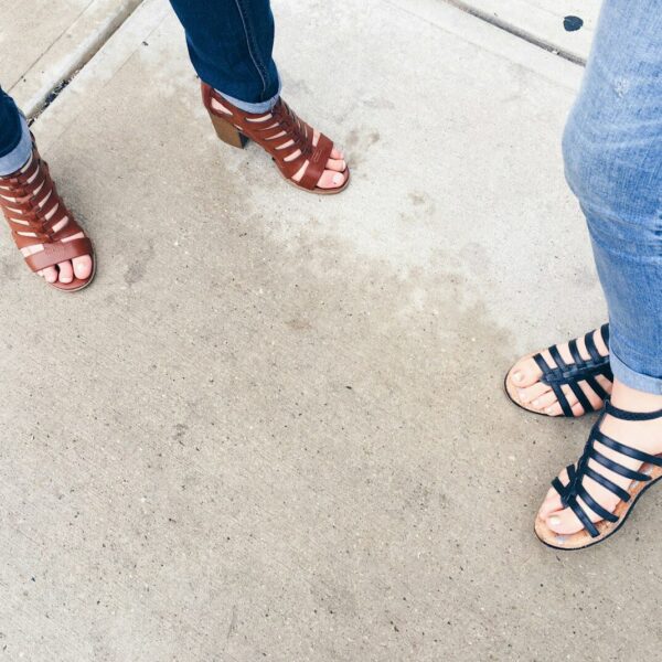two woman wearing black and brown strappy sandals