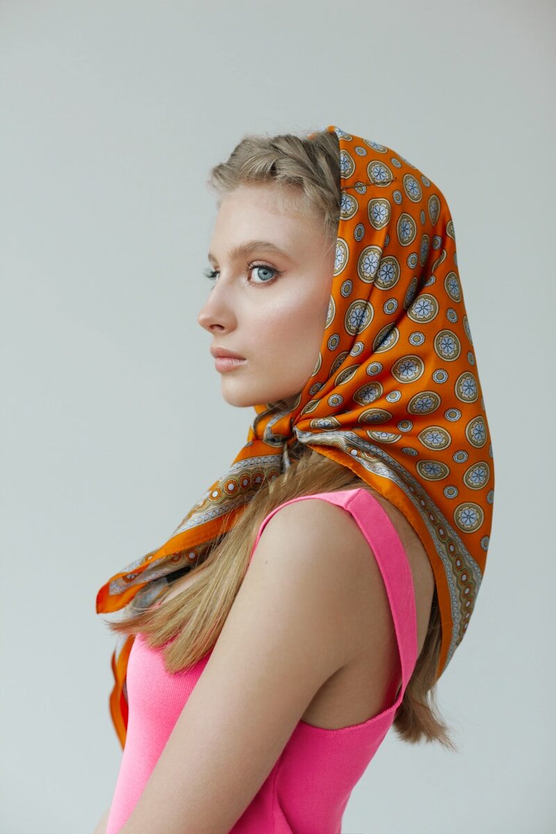 Young woman with orange patterned headscarf and pink dress.