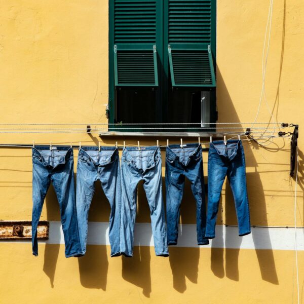 five blue denim jeans hanged on grey cable near window