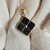 Close-up of a stylish black locket with gold chain on fabric background.