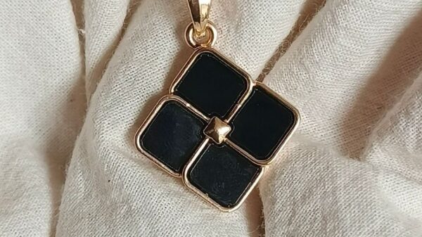 Close-up of a stylish black locket with gold chain on fabric background.