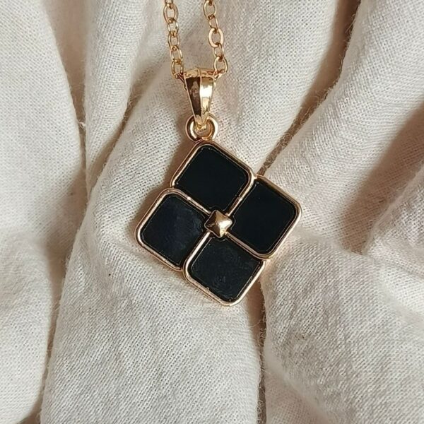 Close-up of a stylish black locket with gold chain on fabric background.