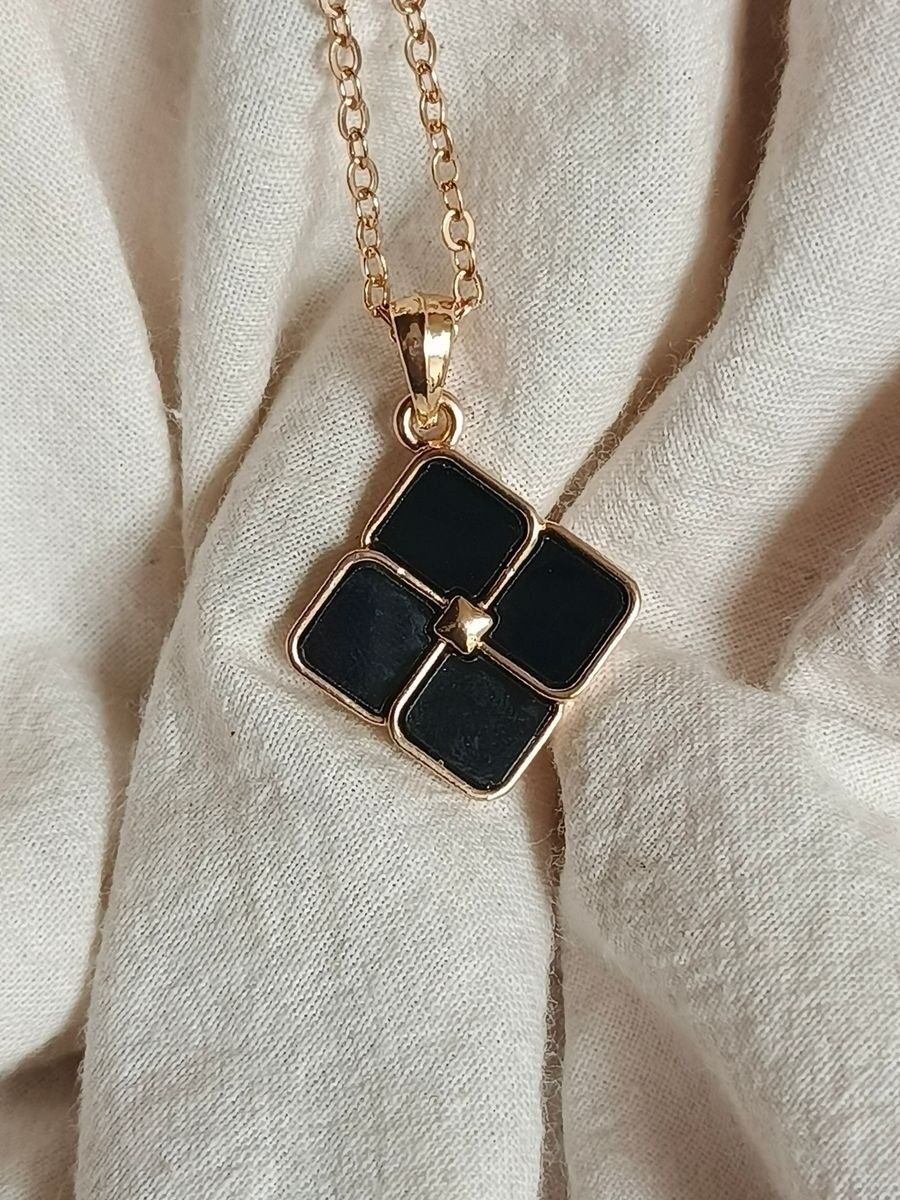 Close-up of a stylish black locket with gold chain on fabric background.