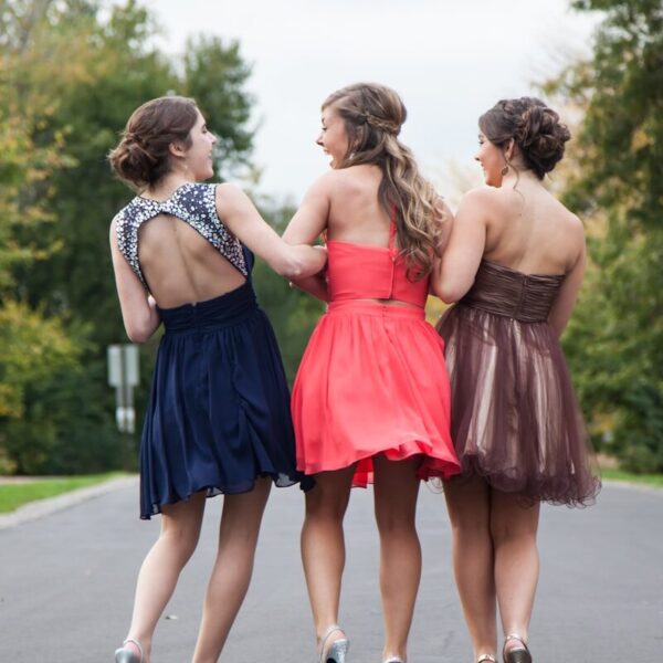 three women wearing red, brown, and blue dresses walking on concrete road during daytime