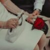 Elegant couple holding hands, one with a red flower wristlet.