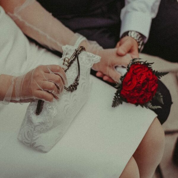 Elegant couple holding hands, one with a red flower wristlet.