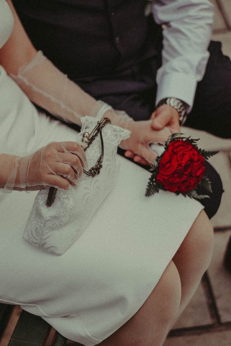 Elegant couple holding hands, one with a red flower wristlet.