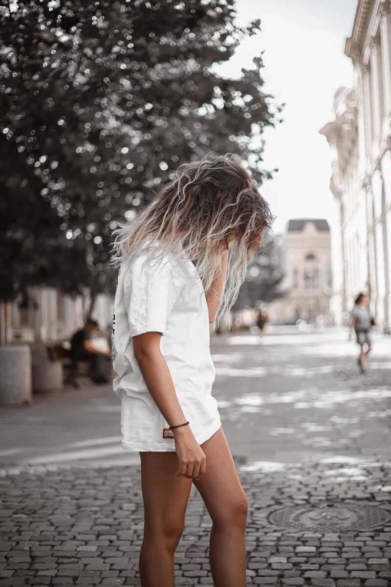 woman in white t-shirt and brown shorts standing on street during daytime