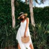 woman in white sleeveless dress wearing brown straw hat standing near green trees during daytime
