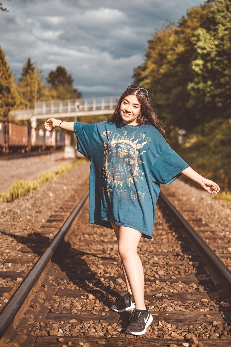 woman in blue long sleeve dress standing on train rail during daytime