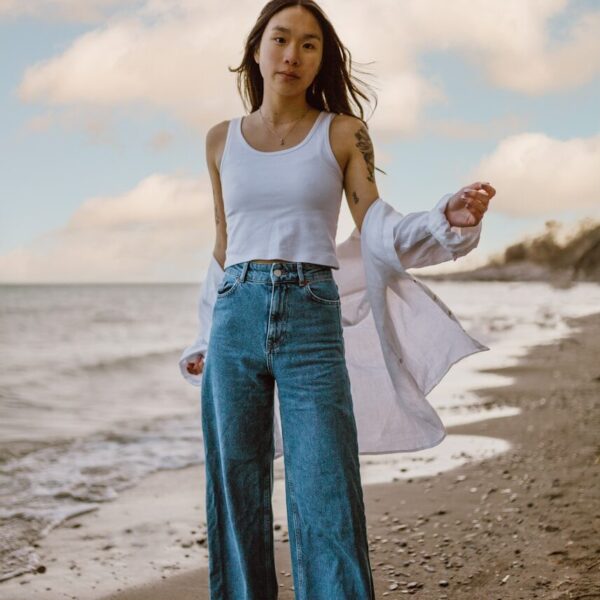 woman in white tank top and blue denim jeans standing on beach during daytime