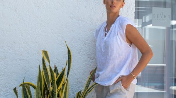 Woman in white top and linen pants by plant.