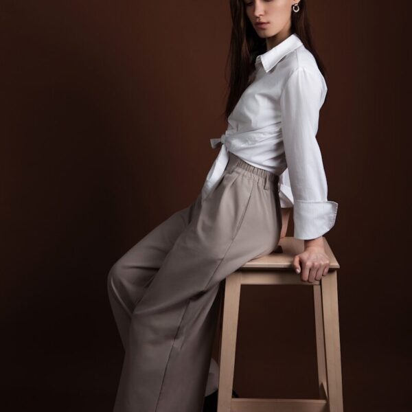 A woman poses elegantly on a wooden stool.