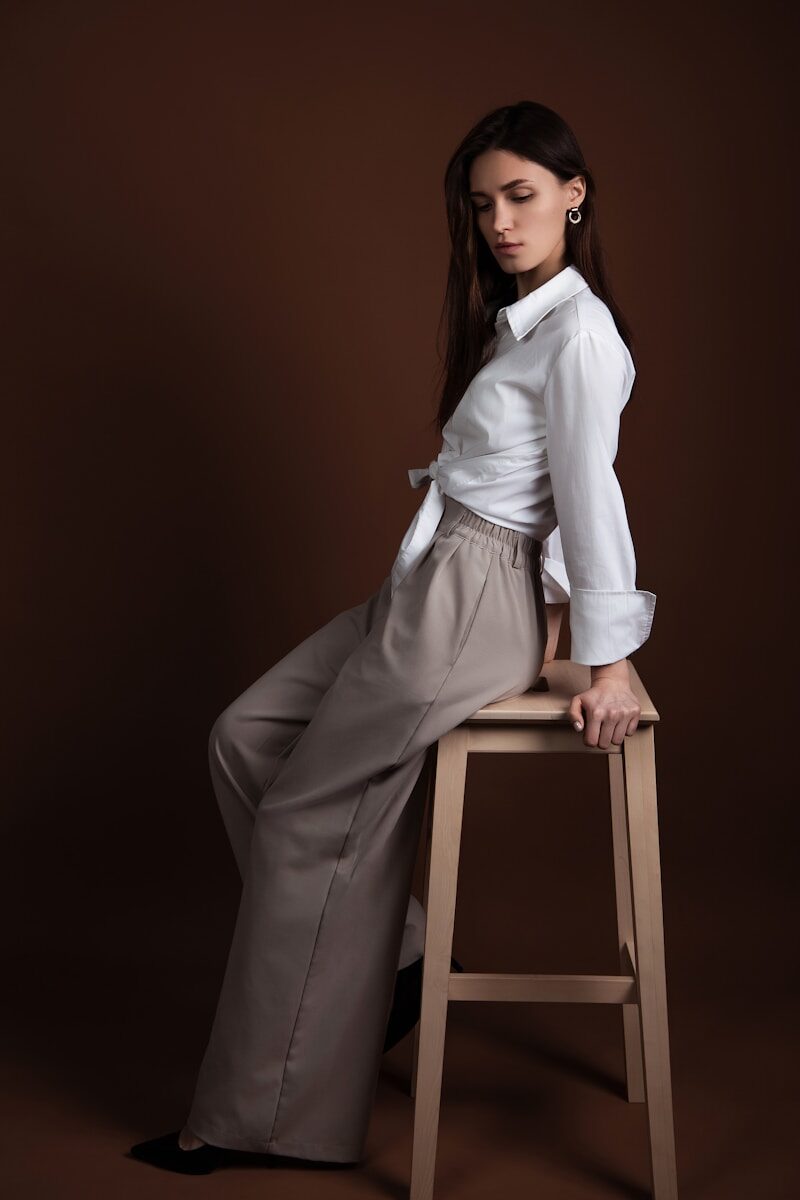 A woman poses elegantly on a wooden stool.