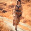 woman in brown and black floral dress standing on dirt road during daytime
