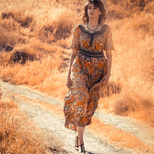 woman in brown and black floral dress standing on dirt road during daytime