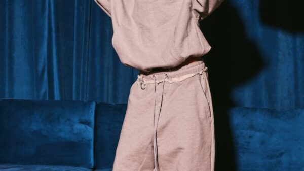 Woman in grey hoodie and pants posing against blue background.