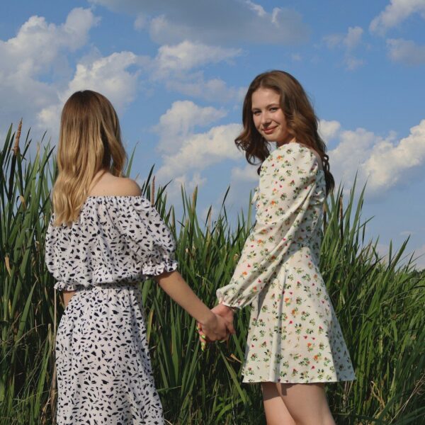 two women holding hands in front of a field of tall grass