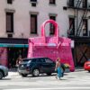 A woman crossing the street in front of a pink bag