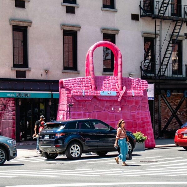 A woman crossing the street in front of a pink bag