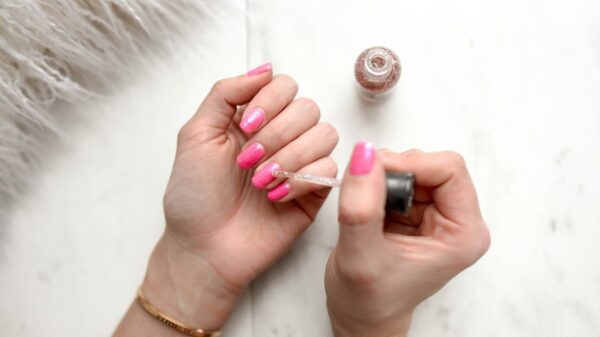 person spreading glittered nail polish on pink nails