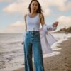 woman in white tank top and blue denim jeans standing on beach during daytime