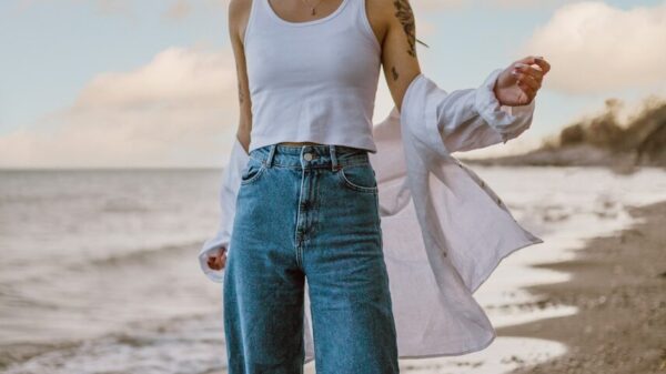 woman in white tank top and blue denim jeans standing on beach during daytime