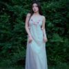 A young woman in a flowing dress stands outdoors.