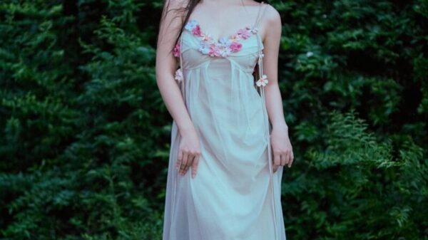 A young woman in a flowing dress stands outdoors.
