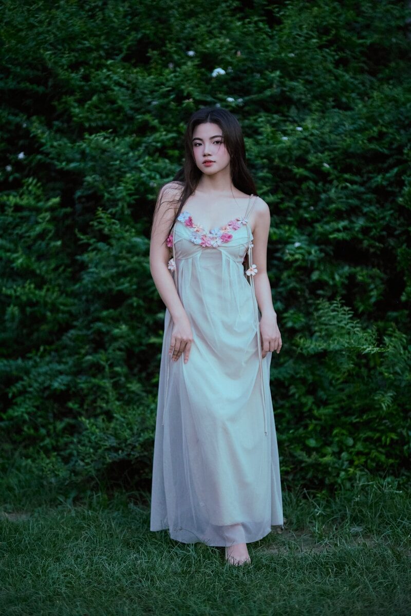A young woman in a flowing dress stands outdoors.