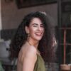 Smiling woman with curly hair wearing an olive green dress.
